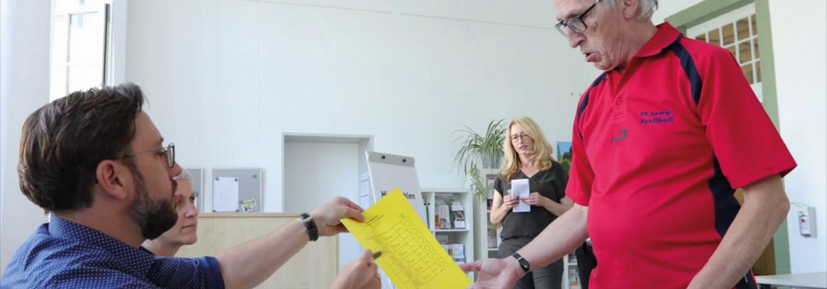 Eine Peron bekommt von einem Wahlhelfer einen Wahlzettel überreicht 