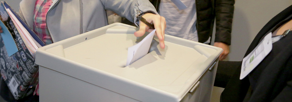 Hand wirft einen Wahlzettel in die Wahlurne