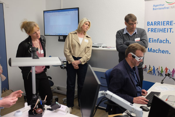 mehere besucher der Ausstellung schauen einem Mann an einem Computerarbeitsplatz über die Schulter