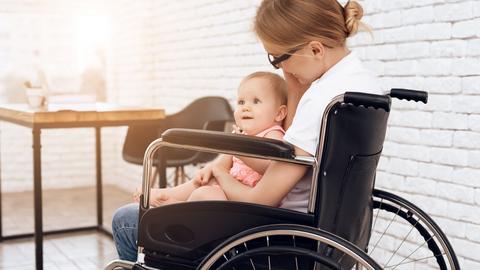 Das Bild zeigt eine Frau im Rollstuhl sitzend mit einem kleinen Kind auf dem Schoß.