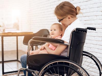 Das Bild zeigt eine Frau im Rollstuhl sitzend mit einem kleinen Kind auf dem Schoß.
