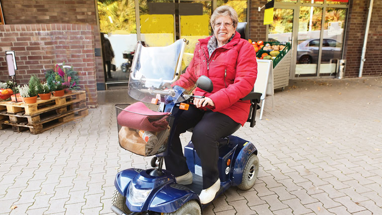 Seniorin auf ihrem Elektromobil vor einem Supermarkt