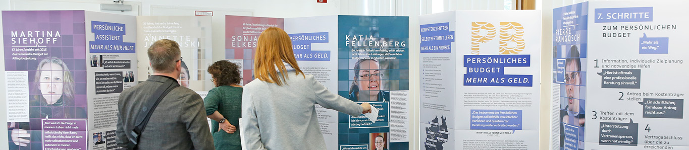 Das Foto zeigt die Wanderausstellung zum Persönlichen Budget und drei Personen, die die Ausstellung betrachten. Die Ausstellung besteht aus vier Elementen. Jedes Element ist ein stehendes Faltdisplay, das Fotos und Texte zeigt. Fünf Personen, die selbst das Persönliche Budget nutzen sind in der Ausstellung porträtiert und ihre Haltung gegenüber dem Persönlichen Budget ist in Zitaten festgehalten. Eine Mitarbeiterin des Landschaftsverbandes Rheinland schildert ihre Erfahrungen mit dem Persönlichen Budget.