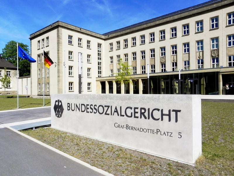 Das Foto zeigt den Eingangsbereich zum Bundessozialgericht. Das Foto zeigt den Eingangsbereich zum Bundessozialgericht. Eingrußes weißes Gebäude. Davor befindet sich eine weiße Tafel mit der Aufschrift Bundessozialgericht.