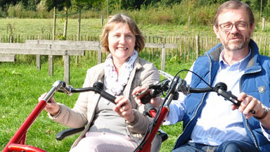 Dreirad-Tandem vor Haus Heidhorn, der NABU-Naturschutzstation Münsterland Ein Dreirad-Tandem wird von einem Mann und einer Frau durch eine ländliche und sonnige Umgebung gefahren